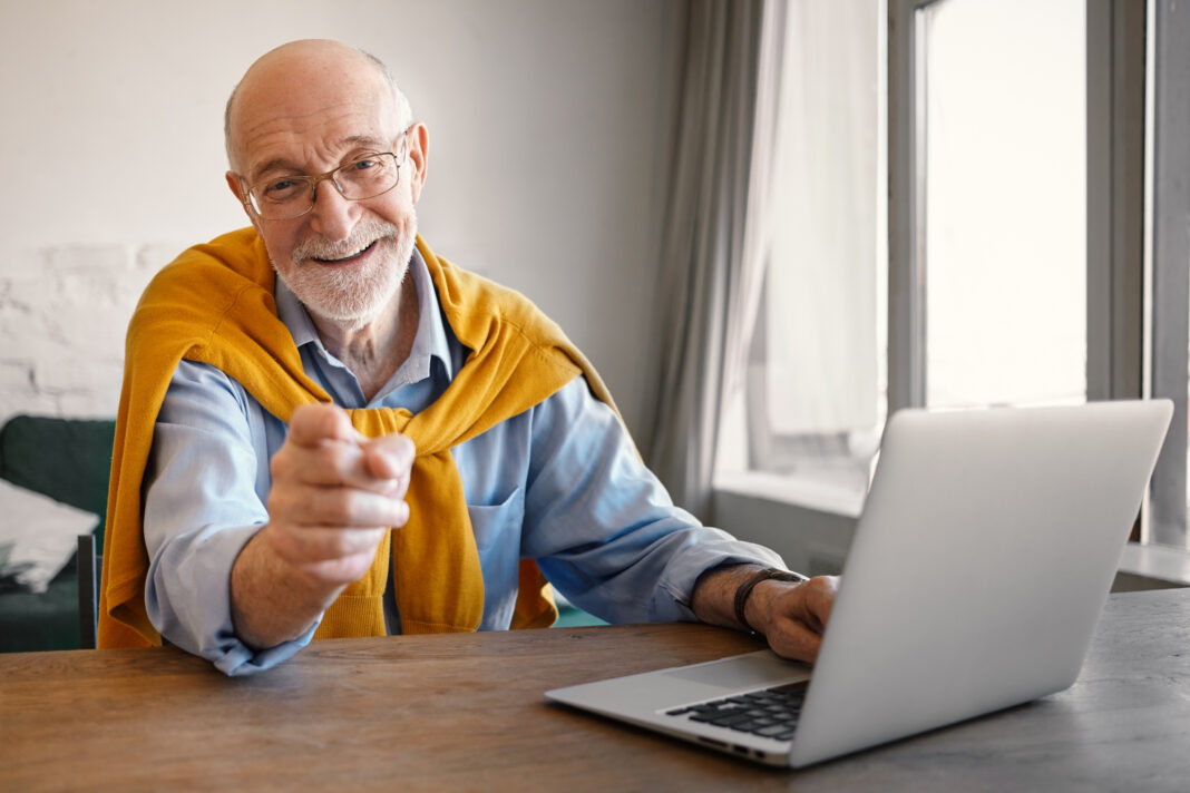 fashionable-friendly-elderly-male-recruiter-wearing-rectangular-glasses-elegant-clothes-working-portable-computer-smiling-broadly-pointing-finger-choosing-you-job-position0
