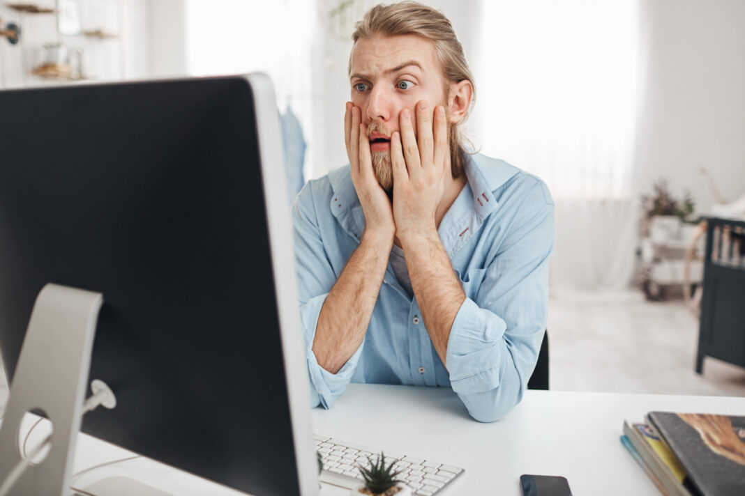 dissatisfied-young-male-manager-looking-with-bugged-eyes-astonishment-shocked-by-financial-report-leaning-elbows-while-sitting-table-front-computer-screen-during-hard-working-day0